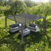 Eine Pergola mit Lamellendach steht auf einer Rasenfläche zwischen Bäumen und bietet mit zwei gepolsterten Sofas und einem Couchtisch einen gemütlichen Außenbereich. Sonnenlicht fällt durch die Blätter und die verstellbaren Dachlamellen.